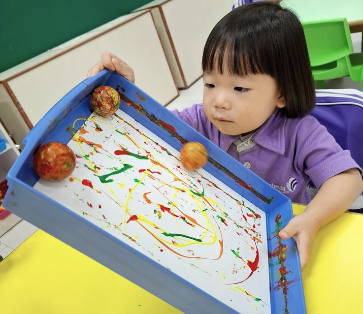 a child holding a board using balls to paint